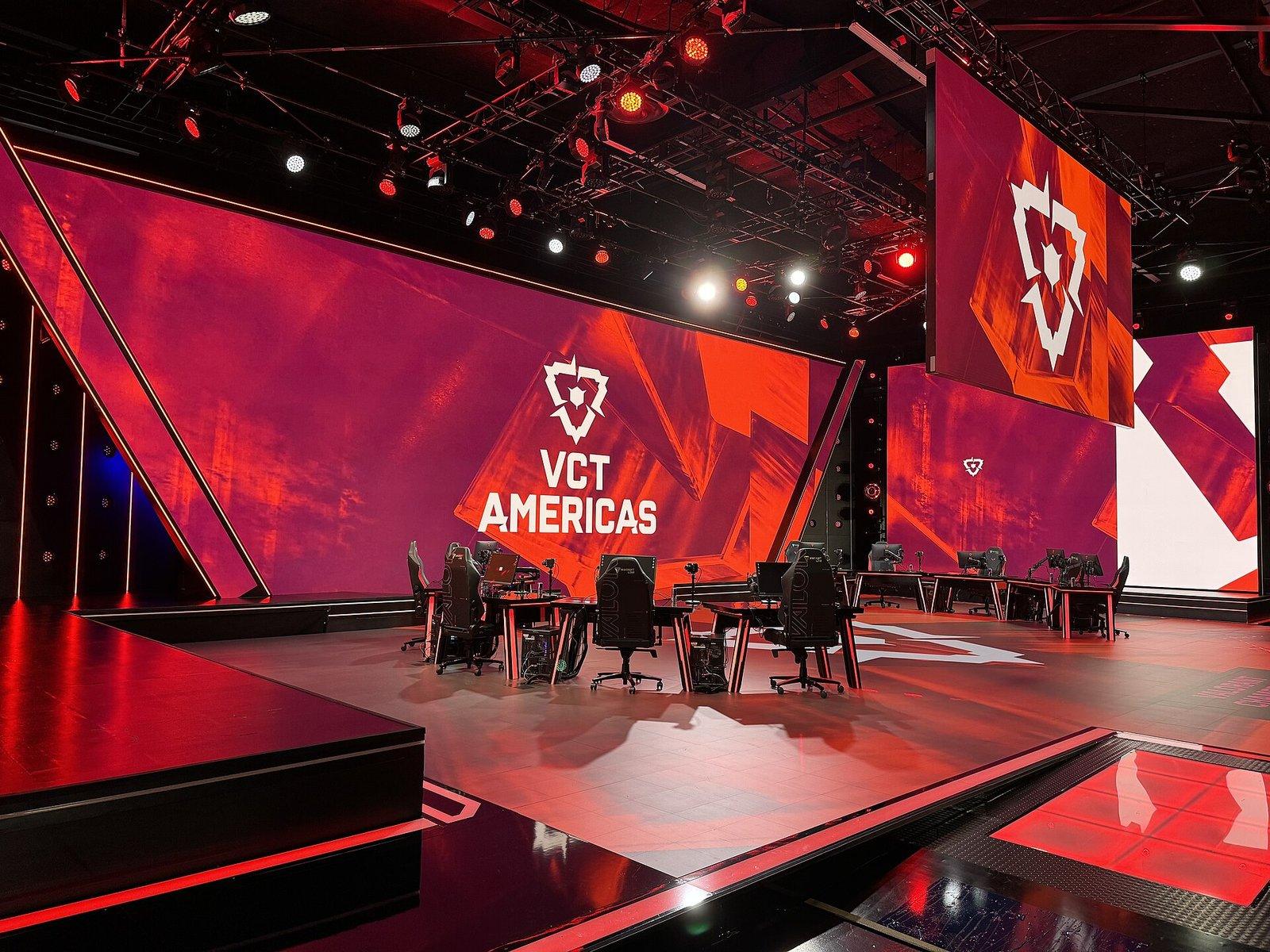 Valorant esports tournament stage at the VCT Americas, with player desks under red lighting